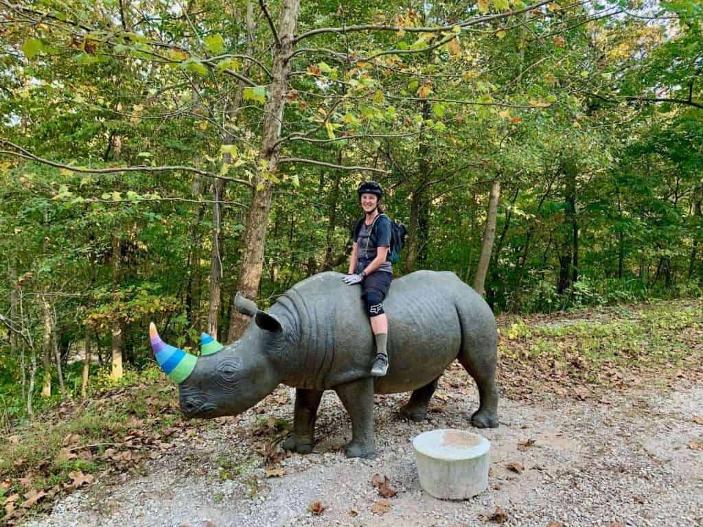Becky sitting atop large fake Rhinoceros with multi-colored horn