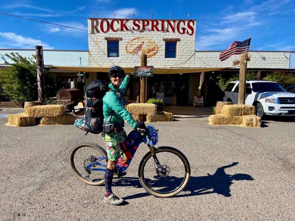 Woman standing over loaded bikepacking bike pointing at Rock Springs cafe sign