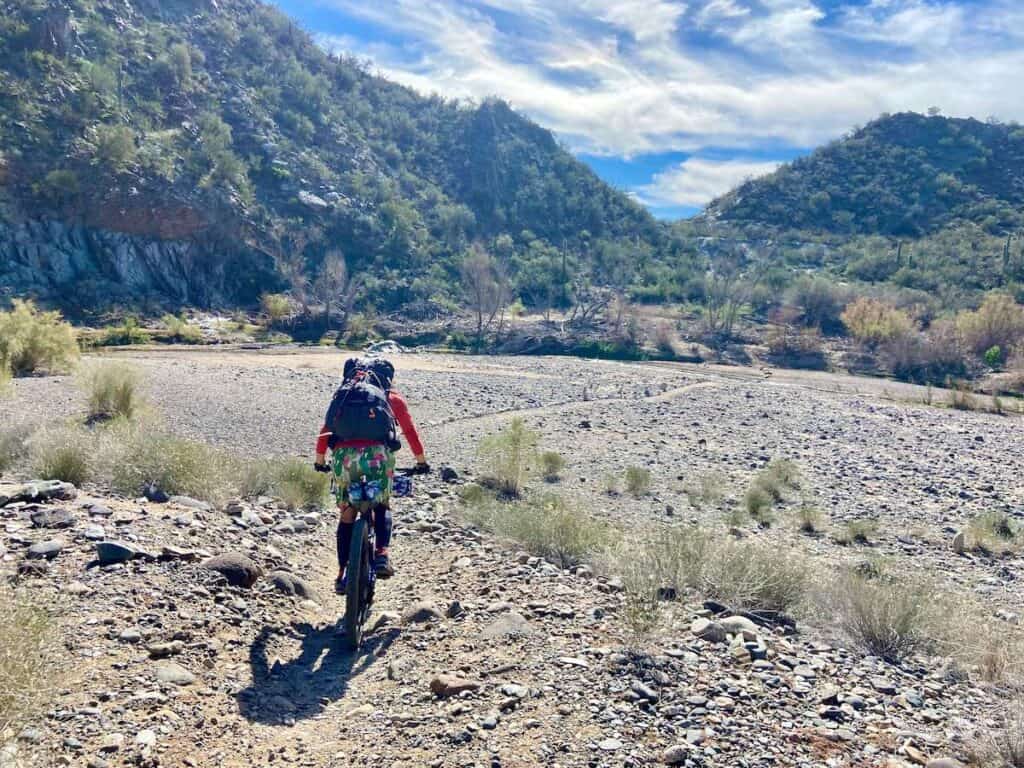 Woman riding bikepacking bike through desert landscape in arizona with mountains ahead