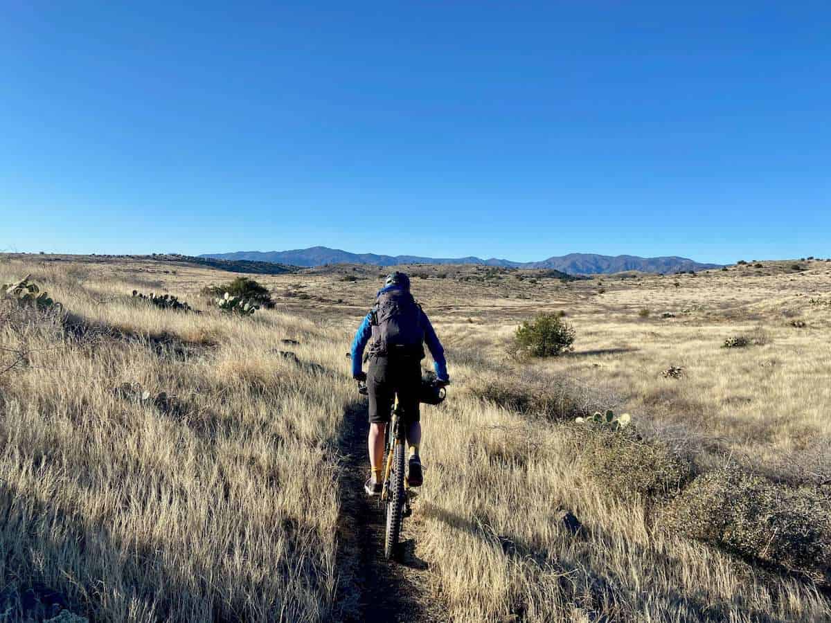 Bikepacker riding bike down singletrack through through dry grassland on the Black Canyon Trail in Arizona