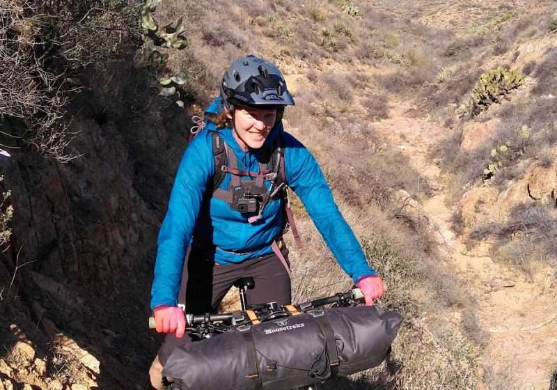 Becky on fully loaded bikepacking bike wearing blue Patagonia Houdini Jacket