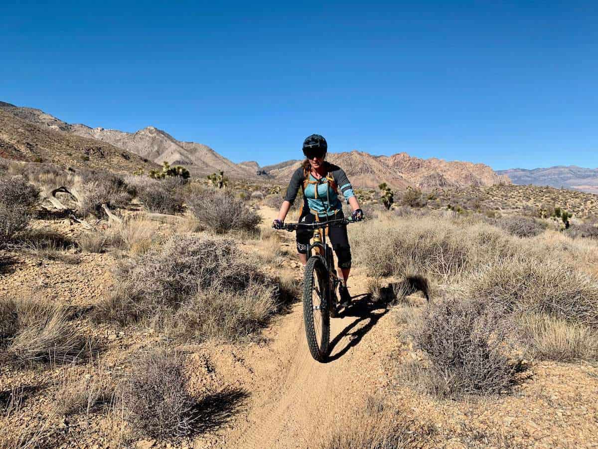 Female mountain biker on desert trail outside of Las Vegas, Nevada. Blue sky overhead and dry sage brush lining trail