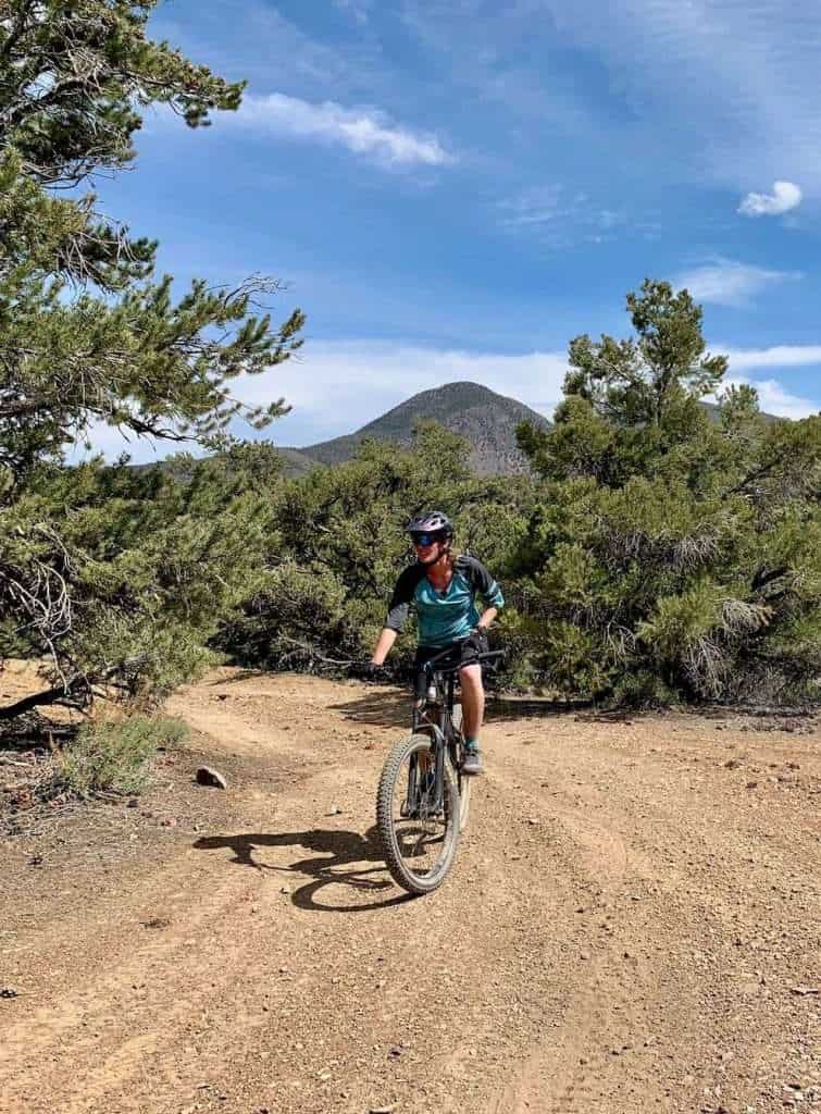 Becky riding mountain bike on doubletrack dirt road lined with pine trees