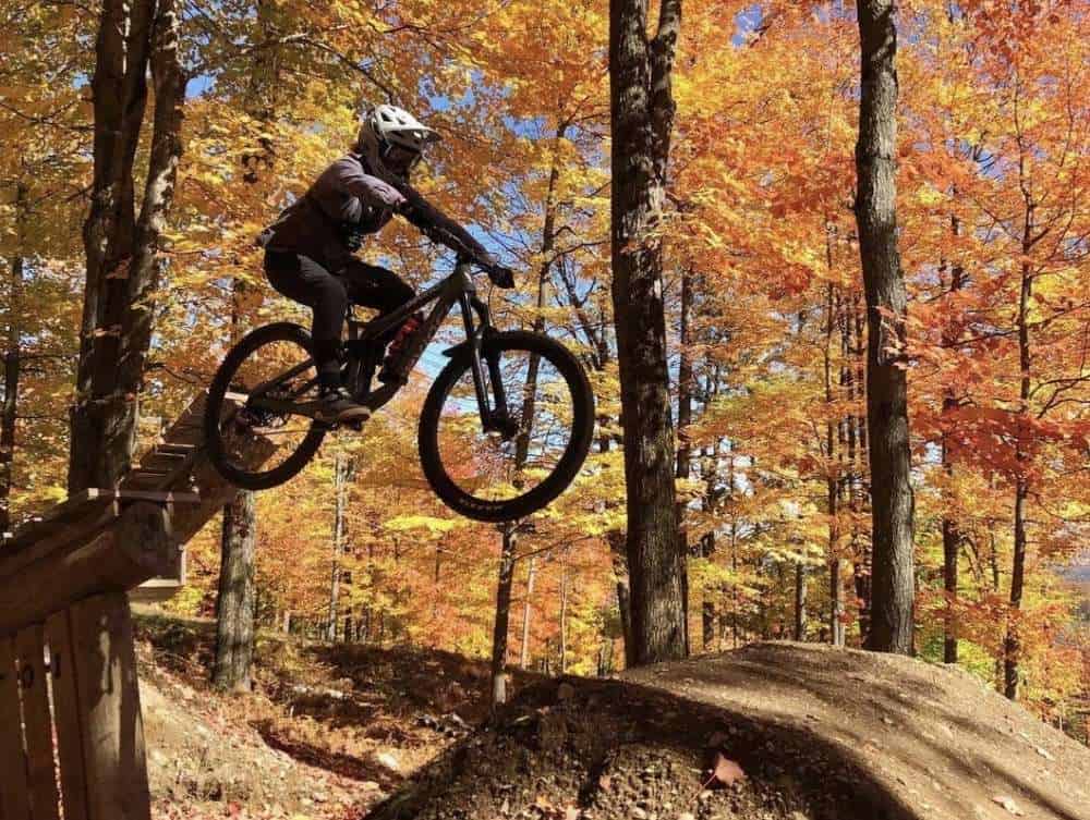 Mountain biking riding off large drop at Bromont Bike Park in Quebec during colorful fall foliage season