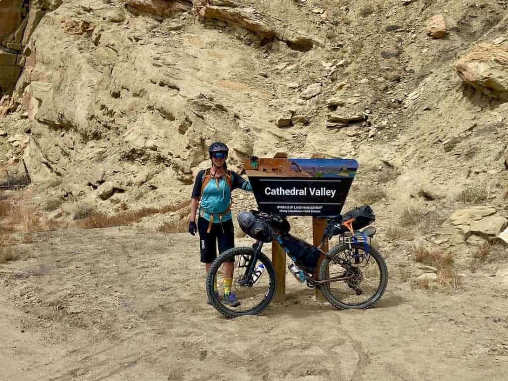 Becky standing next to Cathedral Valley sign with loaded bikepacking bike