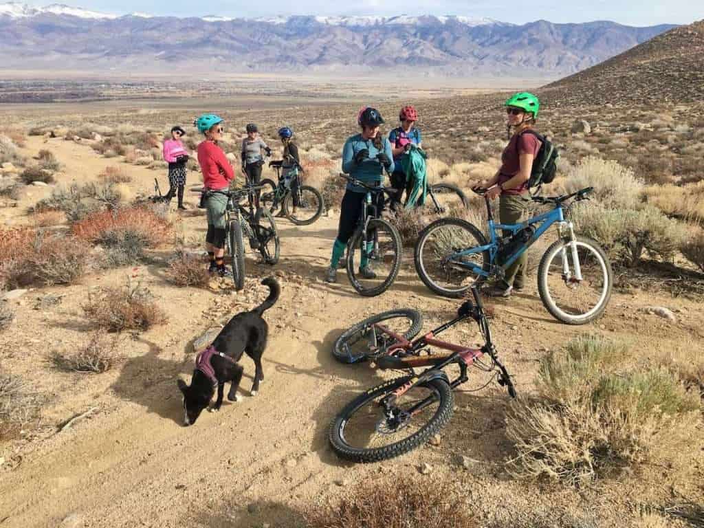 Group of women mountain bikers taking a break on the trail in California with tall snow-capped mountains in the background