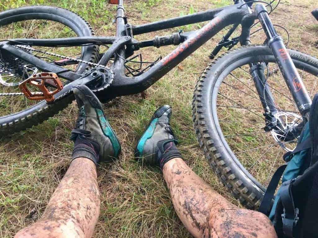 Mountain biker's legs covered in mud with muddy mountain bike lying on ground in front
