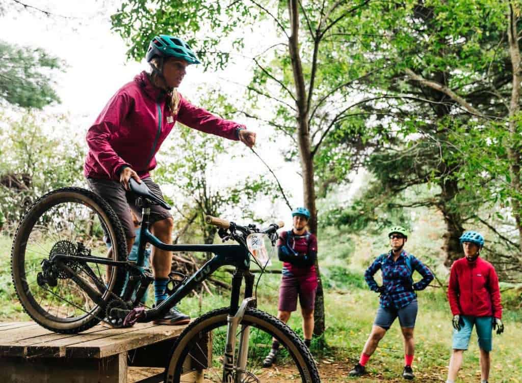 Female mountain bike coach wearing Smith Forefront Helmet while coaching how to go off a low wooden drop