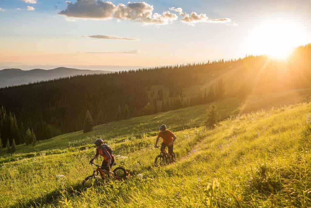Two mountain bikers riding bikes through meadow at Sun Peaks Bike Park in British Columbia at golden hour