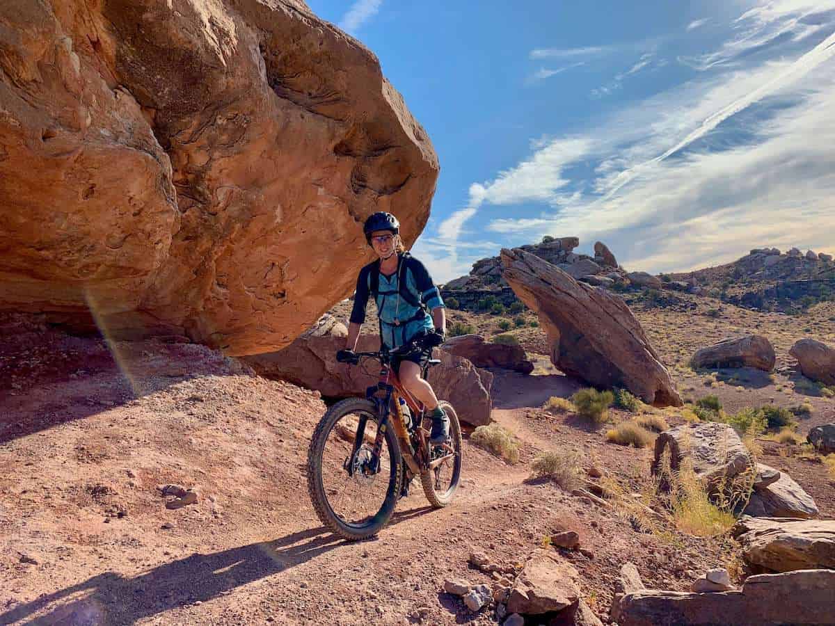 Becky riding mountain bike on singletrack trail in Moab surrounded by red dirt and red rocks
