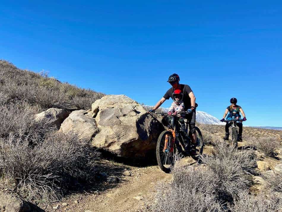 Two mountain bikers riding on singletrack trail each with a child on seat in front