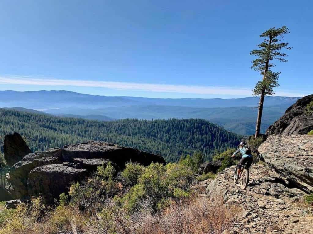 Mountain biker riding around rocky corner on trail in Quincy, California with scenic mountainous landscape in front of her