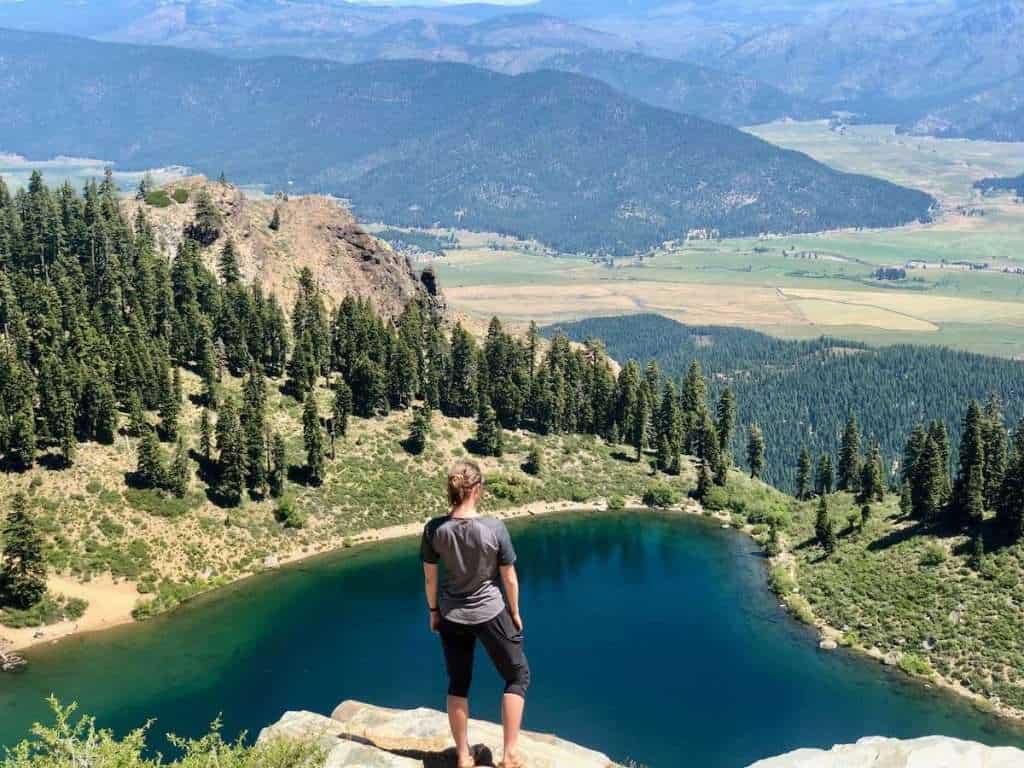 Woman facing away from camera looking out over small lake in northern California from rock ledge high above 
