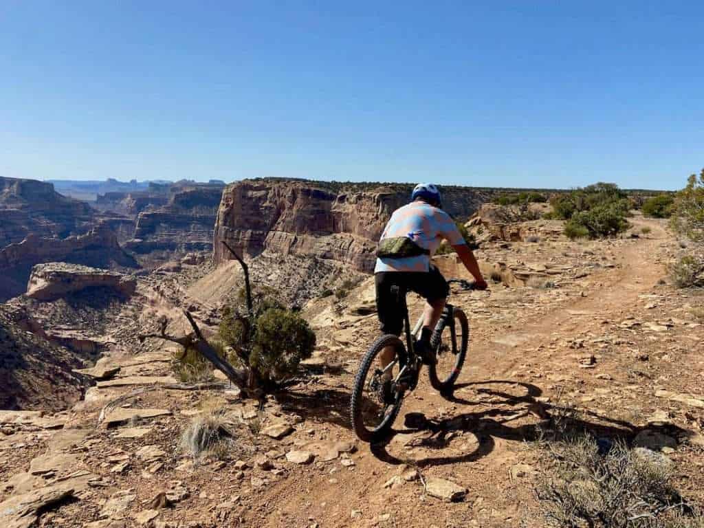 Mountain biker riding on cliffside trail with expansive canyon views in Utah