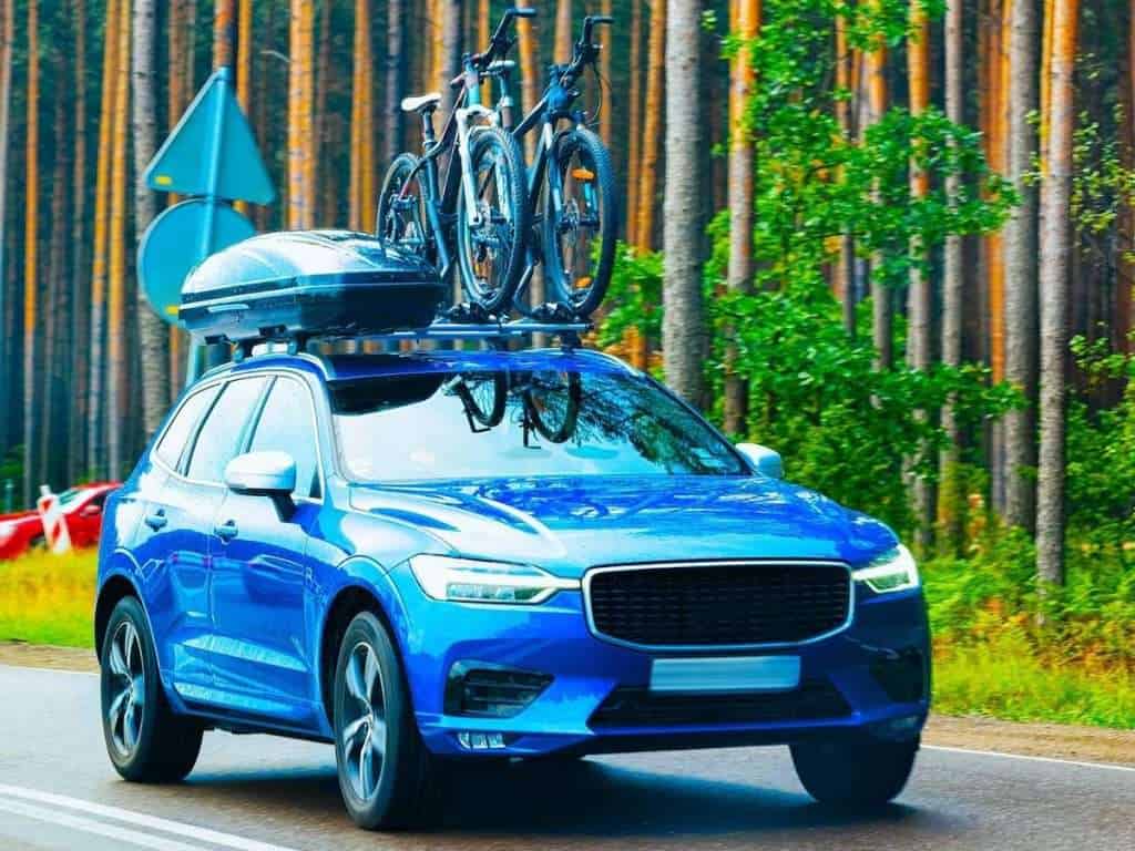 Car driving on road with cargo box and two bikes on roof