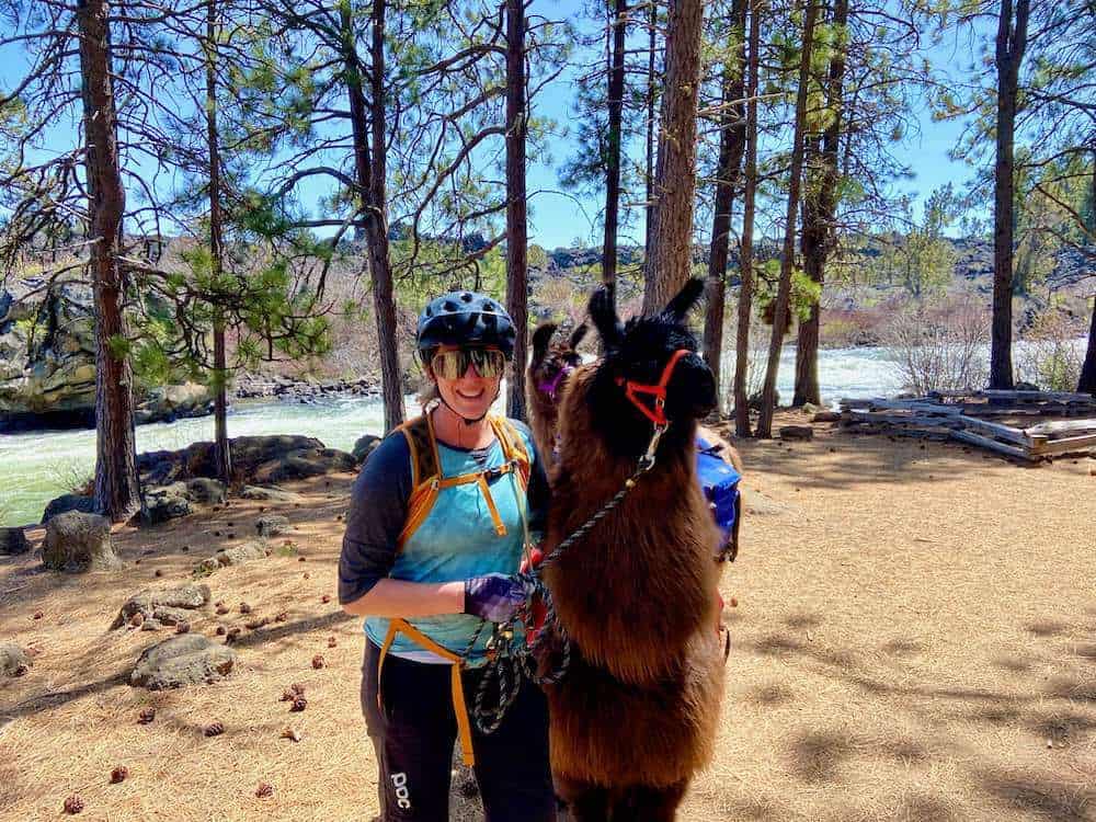 Becky wearing mountain bike gear posing next a llama on the Deschutes River Trail in Bend, Oregon