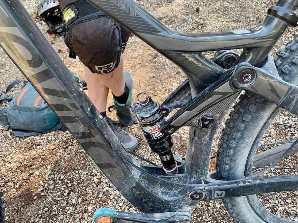 Legs of mountain biker standing behind bike with close up of broken rear shock