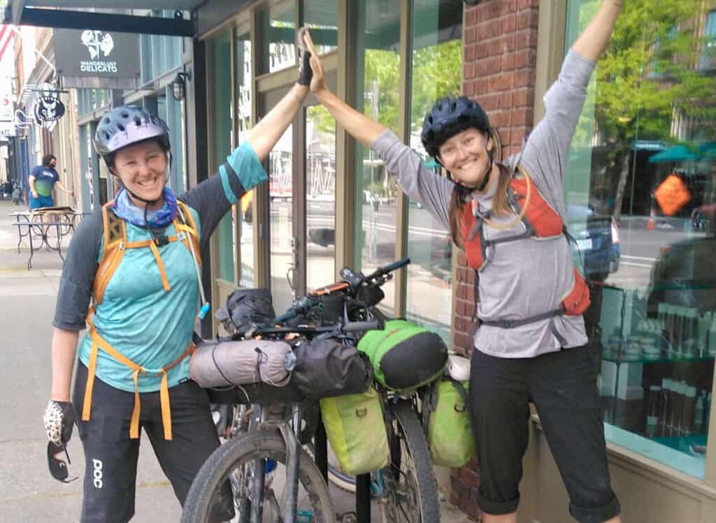 Two female bikepackers giving each other a high five next to loaded bikes after finishing ride across the state of Washington