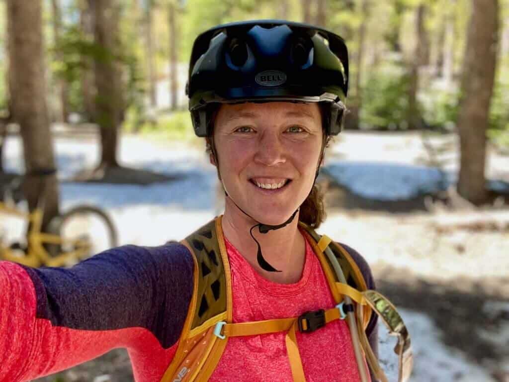 Becky taking a selfie wearing a mountain bike helmet. Patches of snow in the background