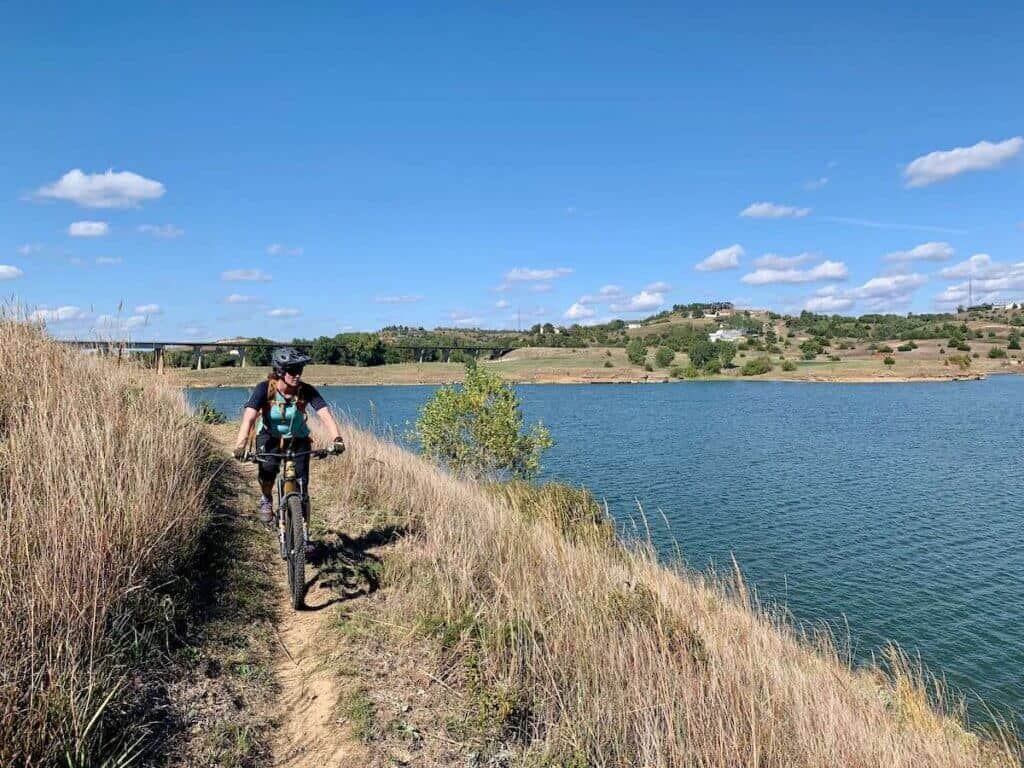 Becky riding mountain biking along singletrack trail next to lake in Kansas