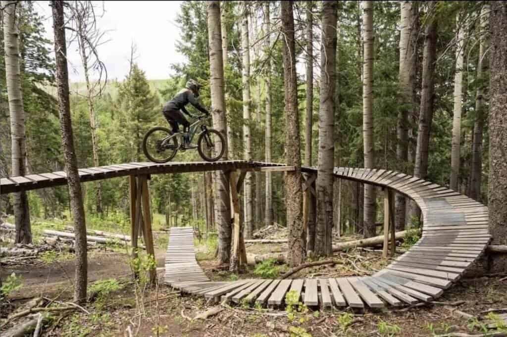 Mountain biker riding on elevated curved wooden ramp features at Pajarito Bike Park in New Mexico