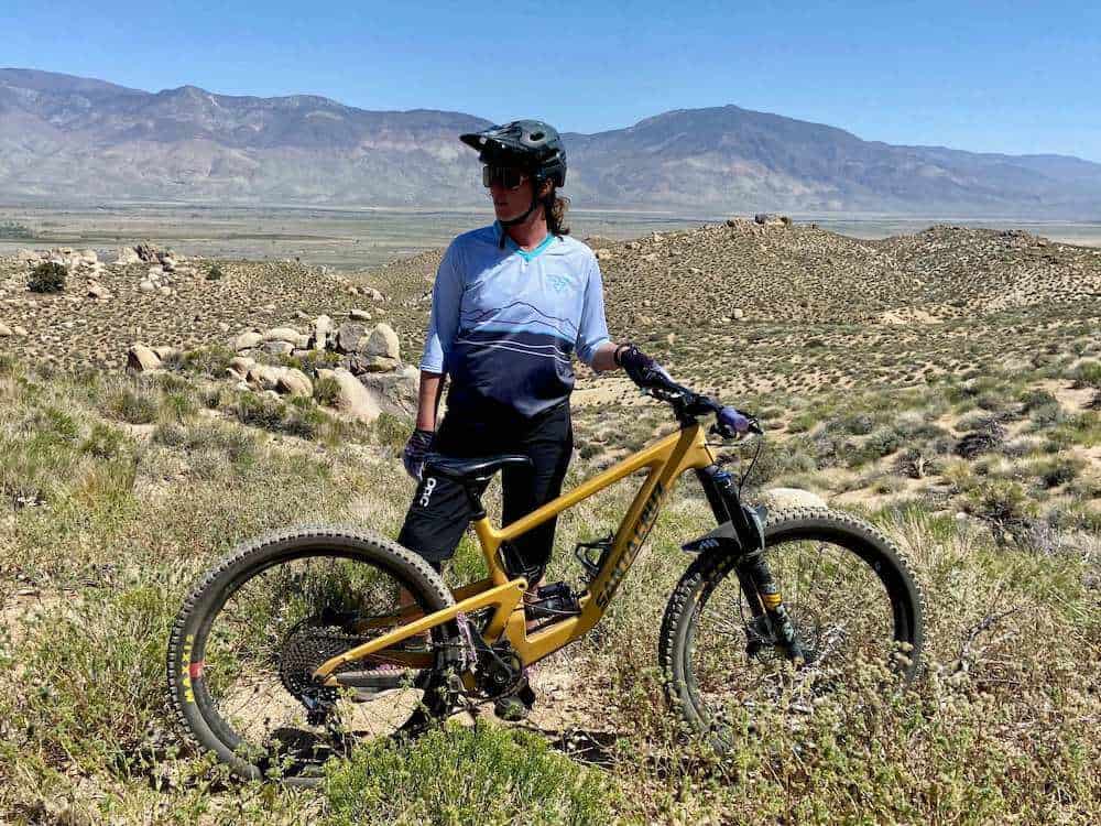 Becky standing behind mountain bike wearing Ride Force mountain bike jersey on high desert trail in California