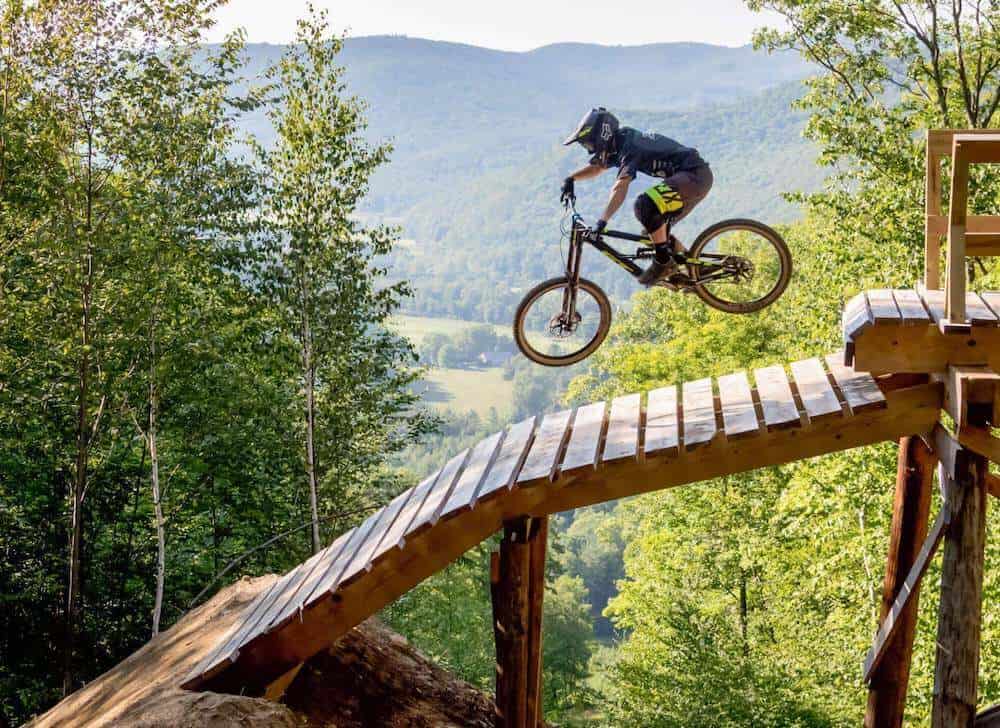 Mountain biker in the air going off wood drop onto wooden ramp at Thunder Mountain Bike Park in Massachusetts
