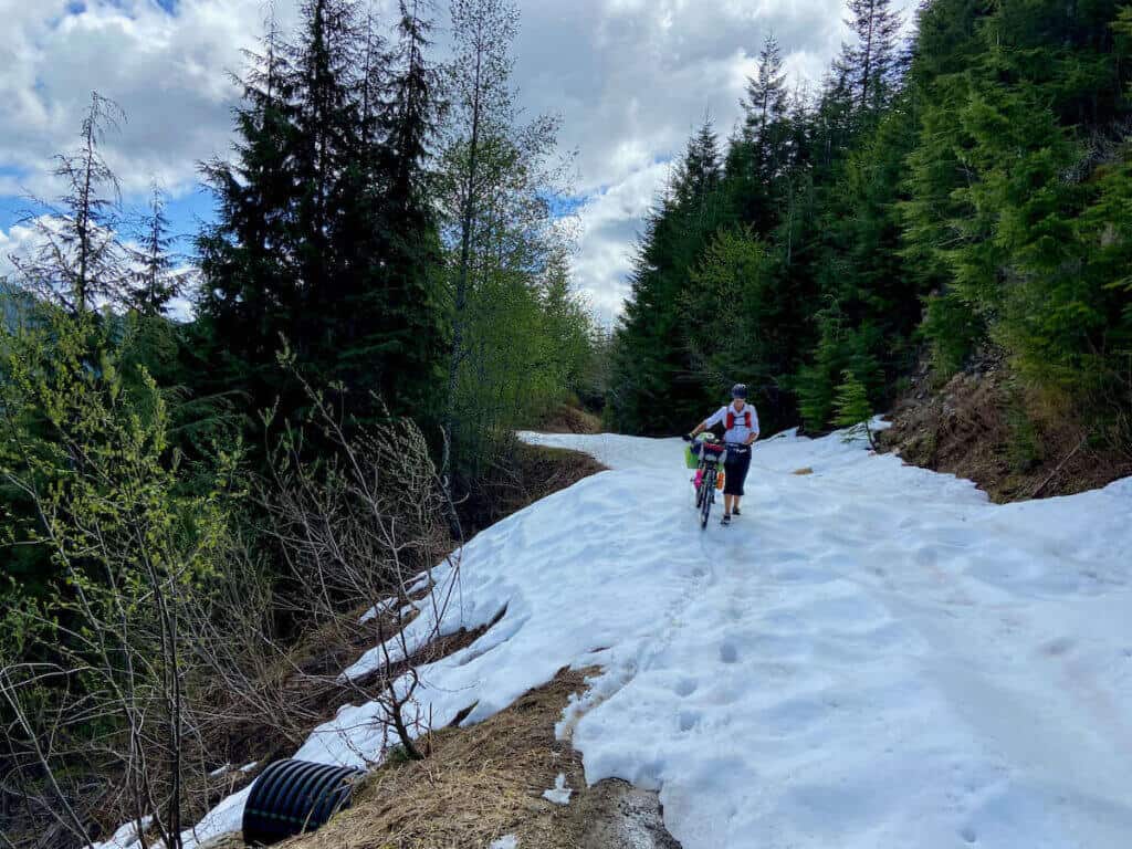 Woman pushing loaded bikepacking bike through snow on the Cross Washington Mountain Bike Route