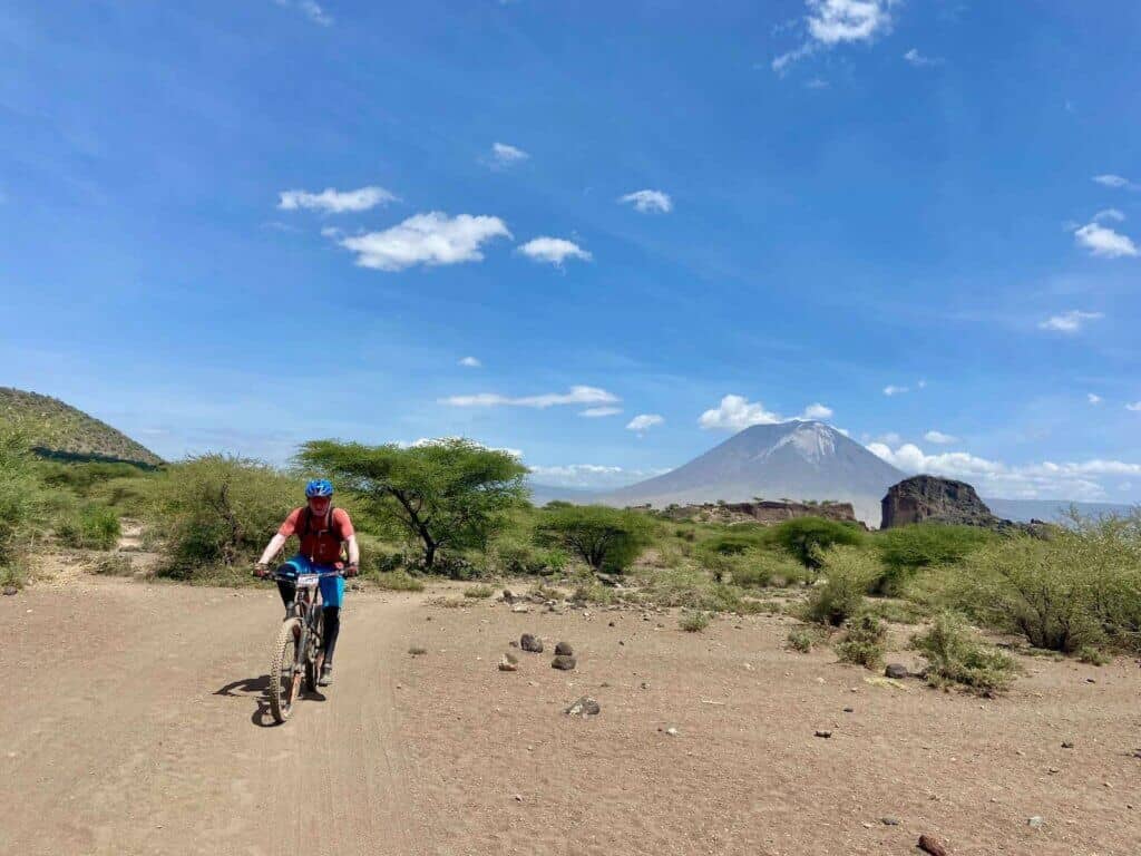 Mountain biker riding bike on sandy track in Tanzania with tall volcano in the distance