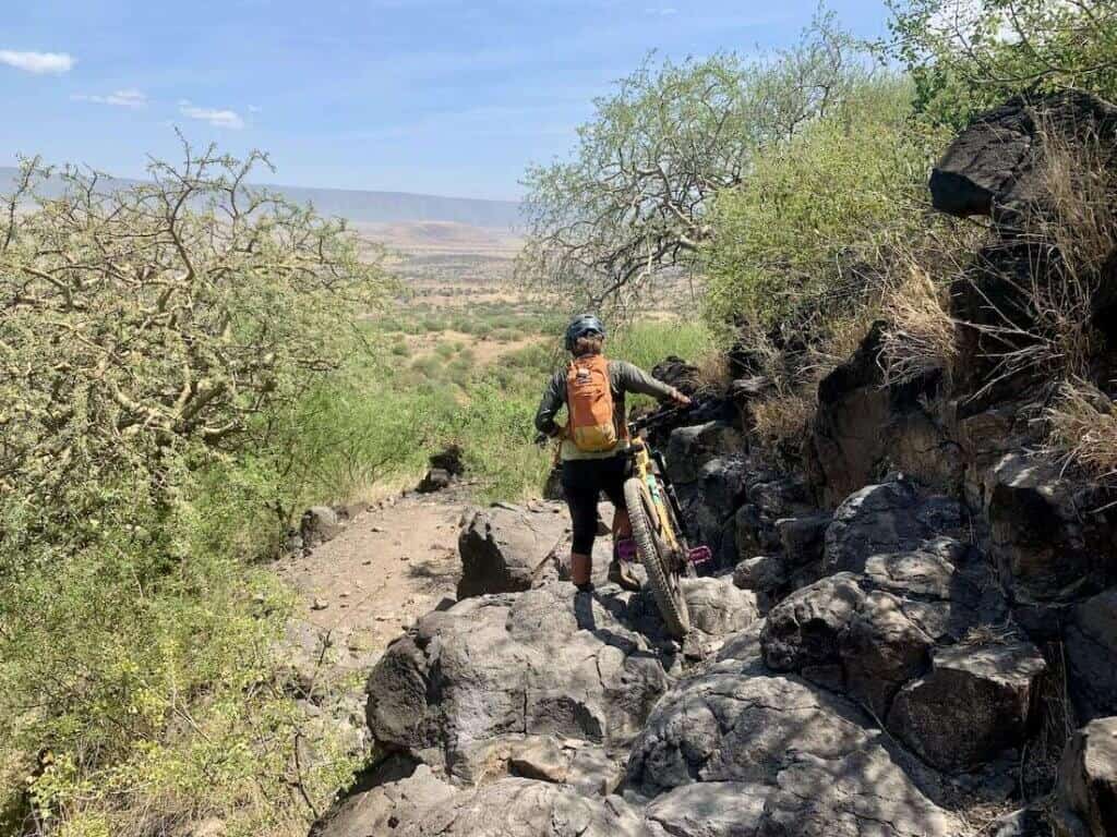 Mountain biker walking bike down over very technical rocky terrain on the K2N mountain bike course in Tanzania