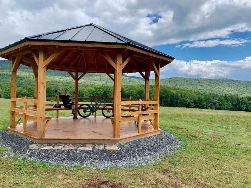 Man sitting next to bike in wooden gazebo in Vermont with pasture and rolling hills in background