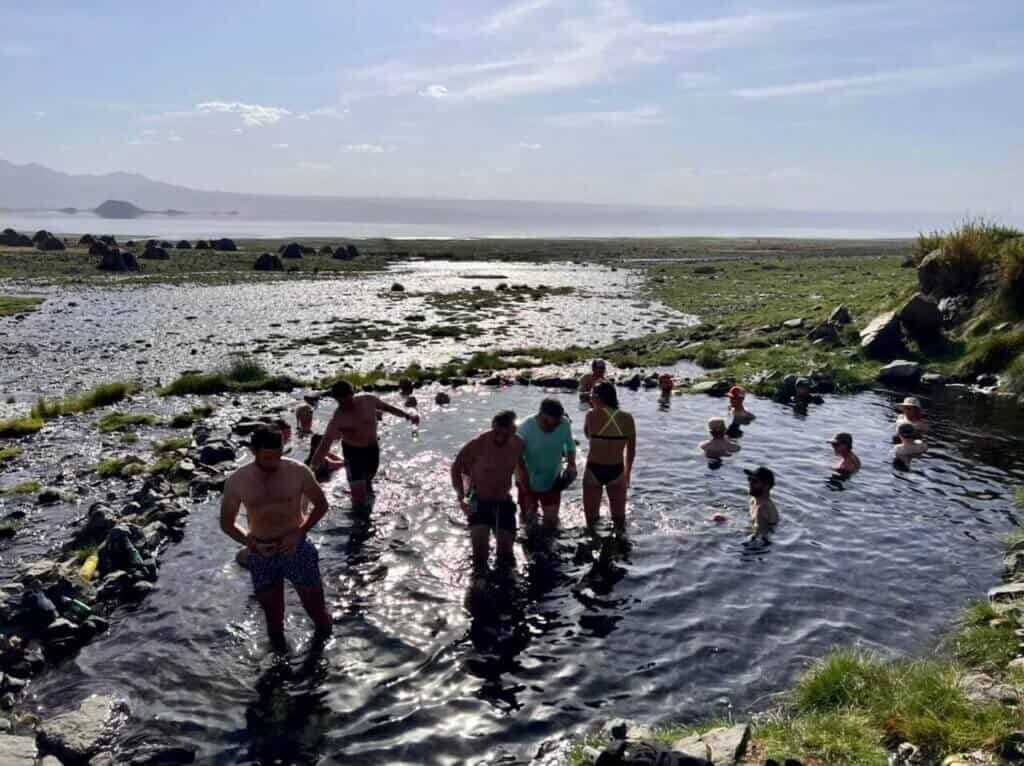 Group of people sitting and standing in shallow natural hot tub pool near the shores of Lake Natron in Tanzania