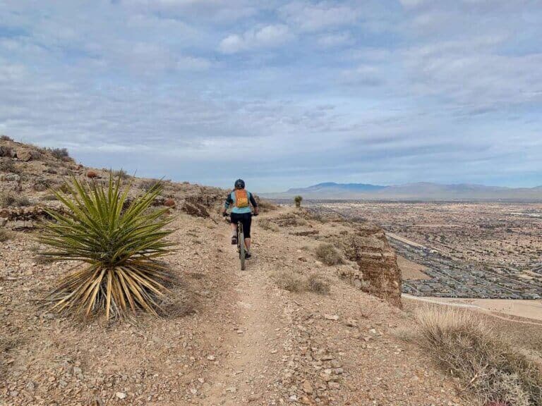 Becky riding bike on singletrack trail above views of Las Vegas, Nevada