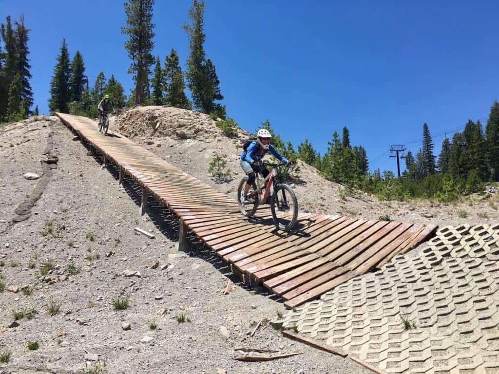 Two mountain bikers riding down wooden ramp at bike park in California