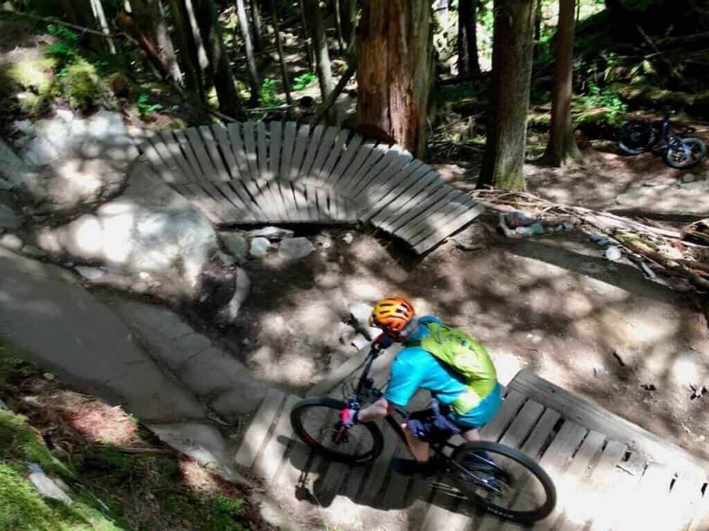 Mountain biker riding down manmade curved ramp on mountain bike trail in Squamish, British Columbia