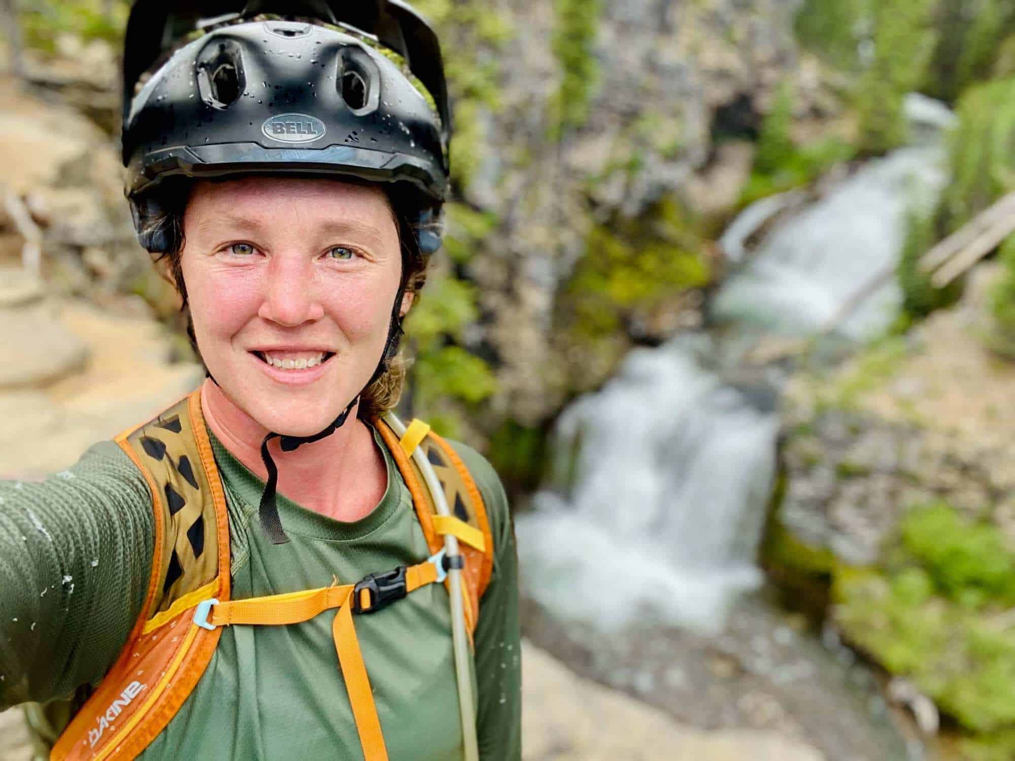 Portrait selfie of Becky with mountain bike gear on in front of waterfall in Oregon