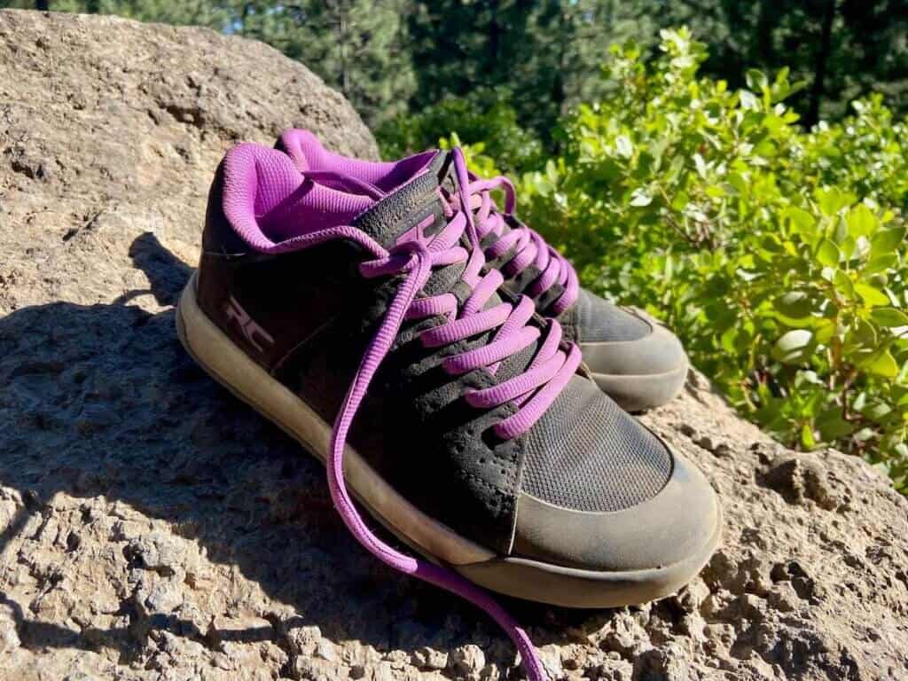 Pair of women's Ride Concepts Livewire shoes with purple laces displaced on a rock