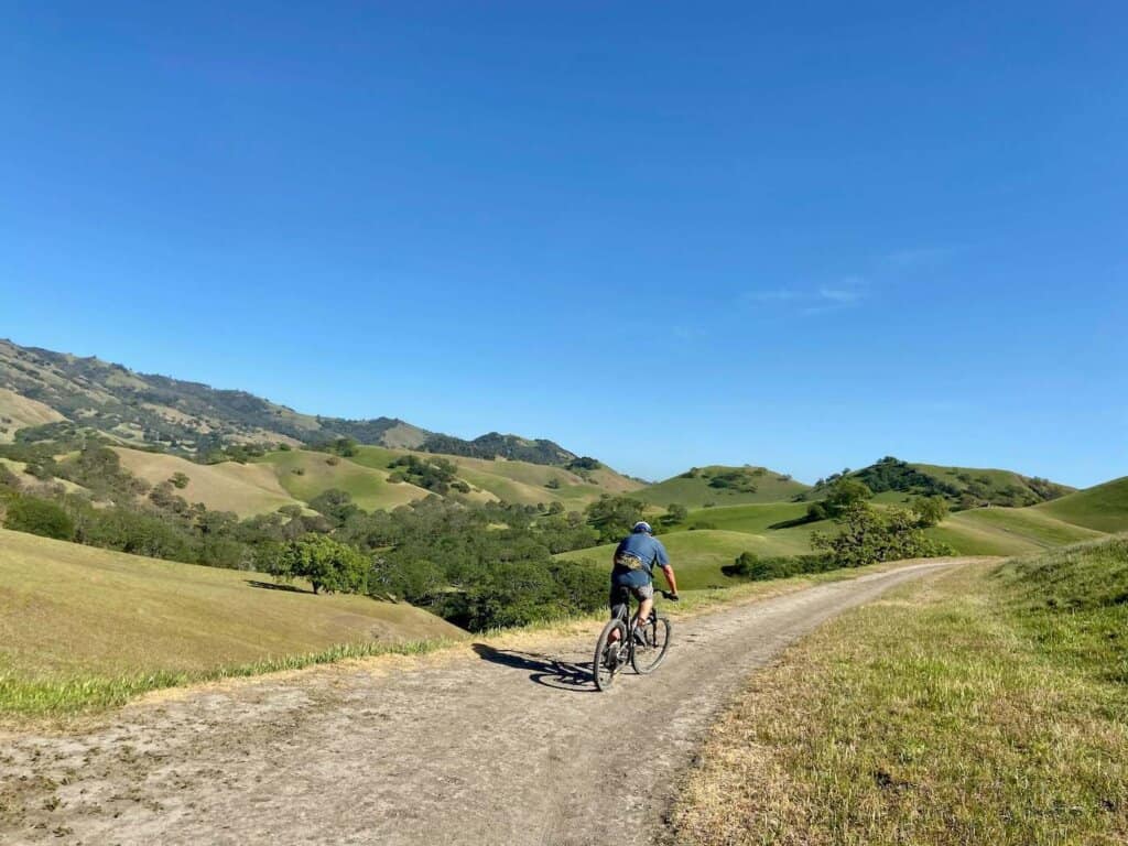 Mountain biker riding along doubletrack road through lush green hills outside of San Francisco