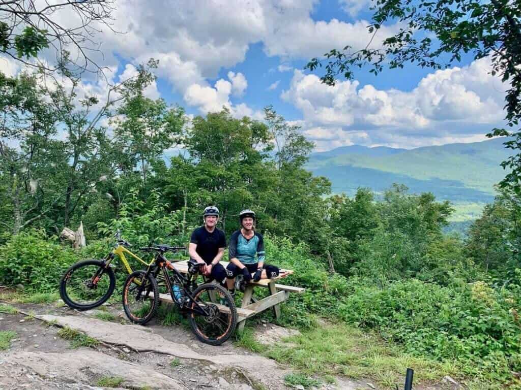 Becky and her dad sitting on picnic table at vista lookout in Vermont with mountain bikes