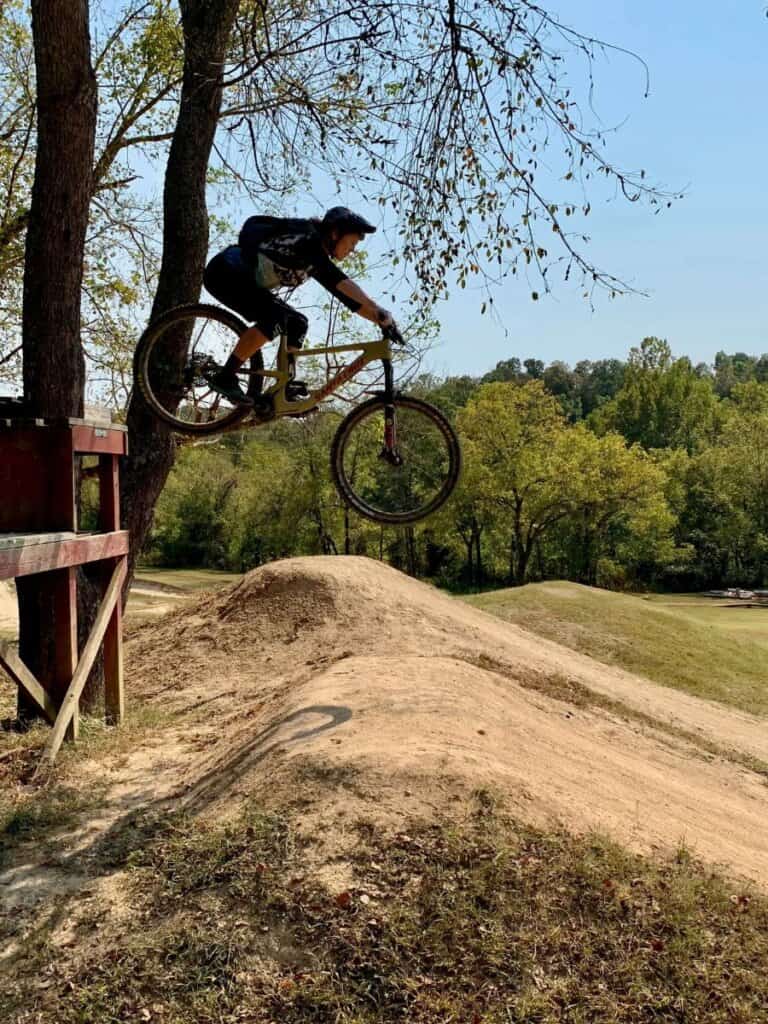 Becky riding off bike wooden ramp and drop on mountain bike at the Slaughter Pen Trails in Bentonville, Arkansas