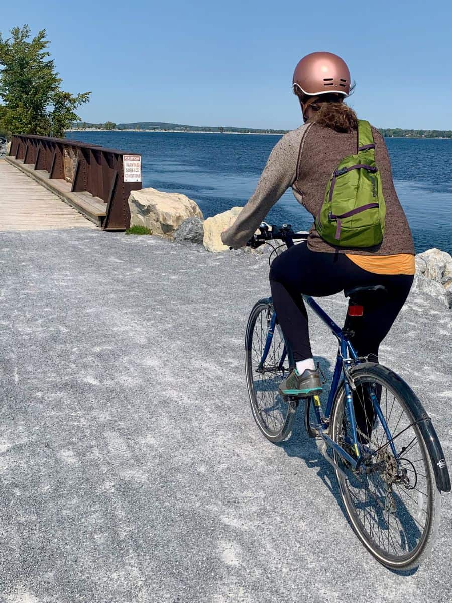 Becky riding bike on gravel Burlington Bike Park in Vermont with Lake Champlain on right sie