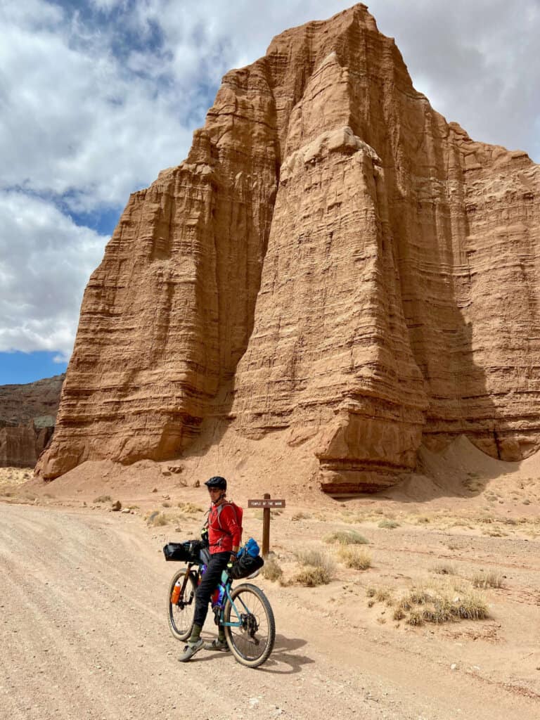 Bikepacker riding bike on remote dirt road in Monument Valley in Capitol Reef National Park with towering monolith behind her