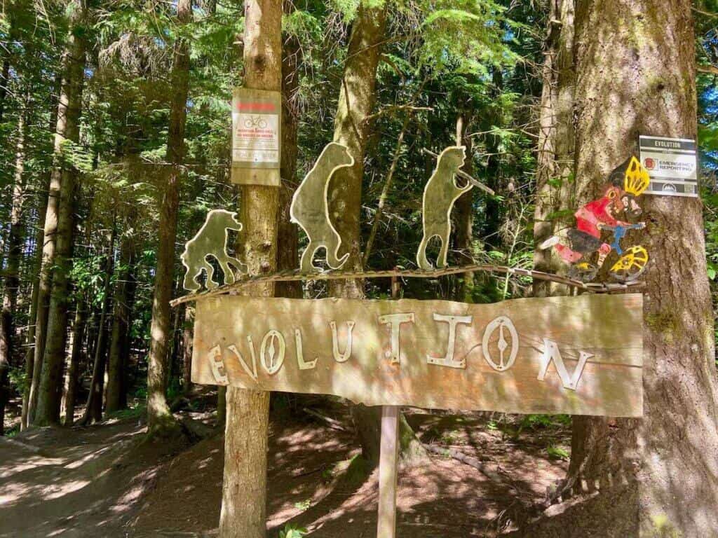 Mountain bike trail sign at Galbraith Mountain for Evolution trail with figures of apes turning into a mountain biker