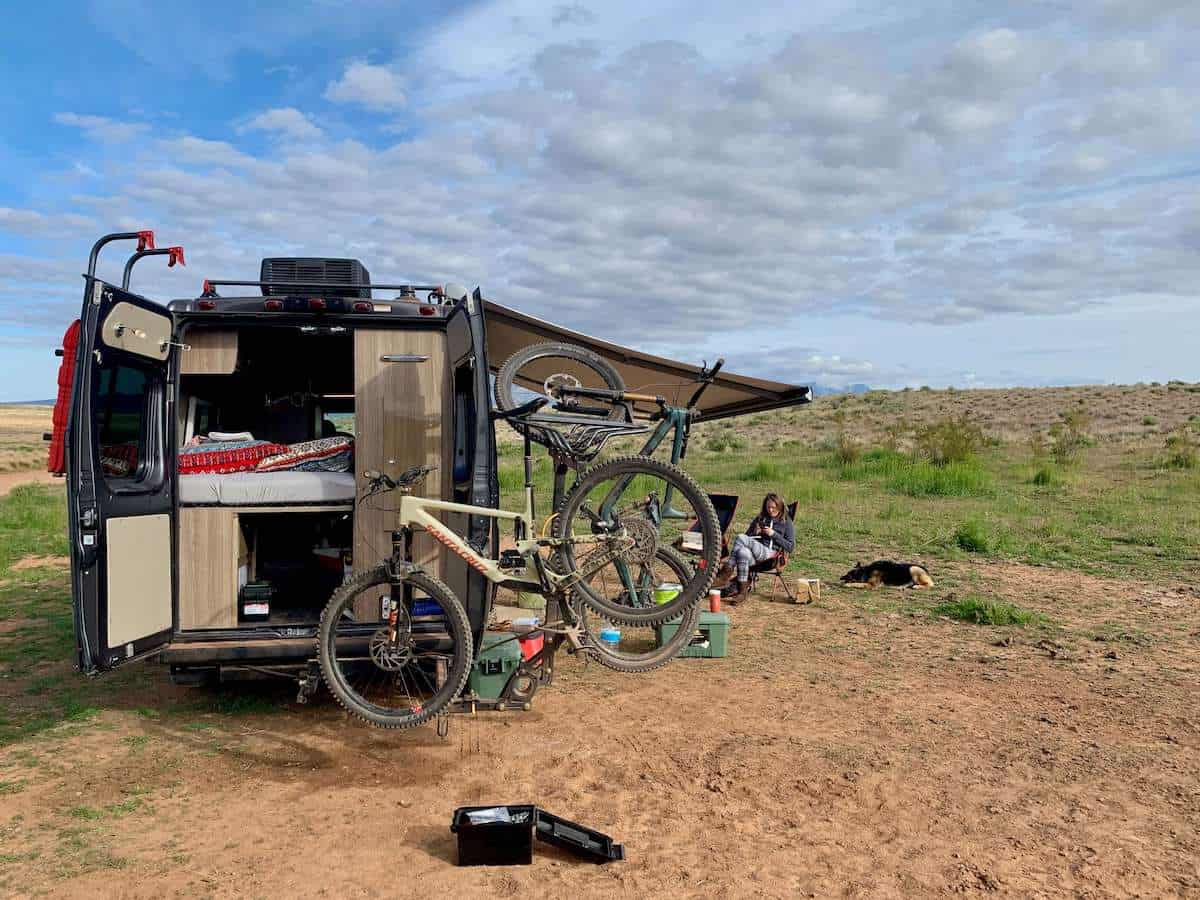 Photo of back of converted van with doors open and mountain bike on bike stand. Van is parked in remote dispersed campsite