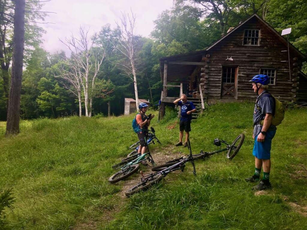 Three mountain bikers standing in front of log cabin in Vermont