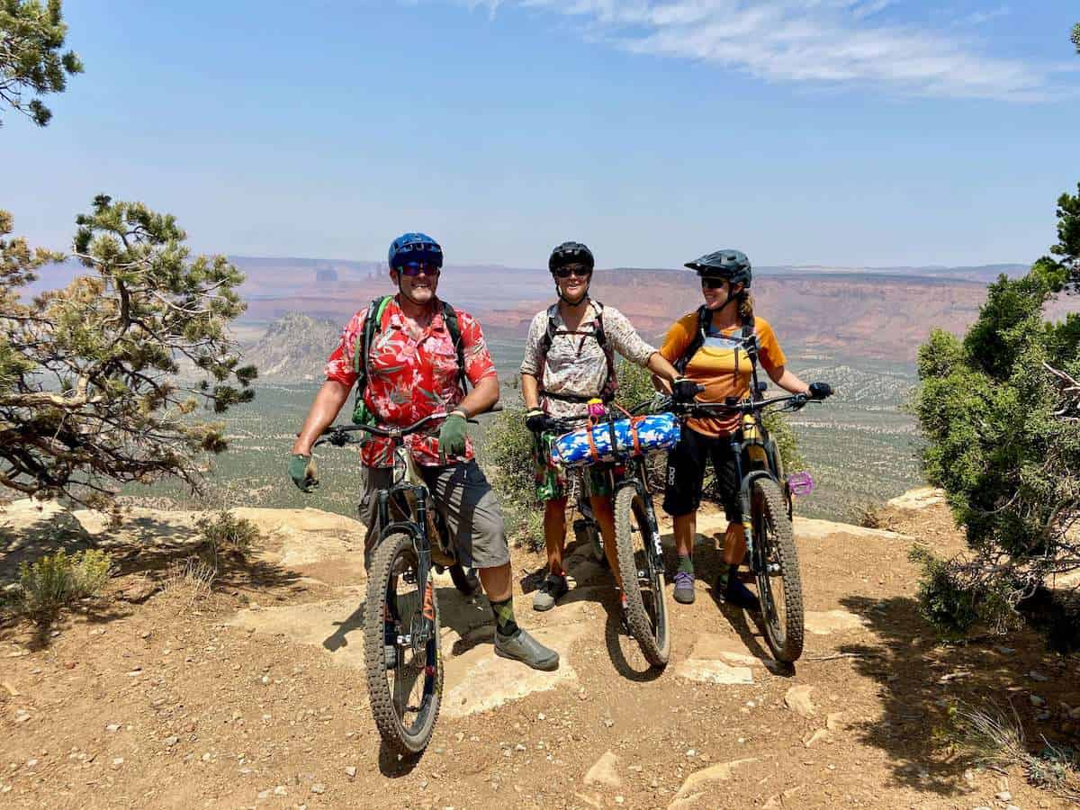 Three mountain bikers posing for photo with dramatic canyonland landscape in background on the San Juan Moab to Telluride hut to hut mountain bike trip