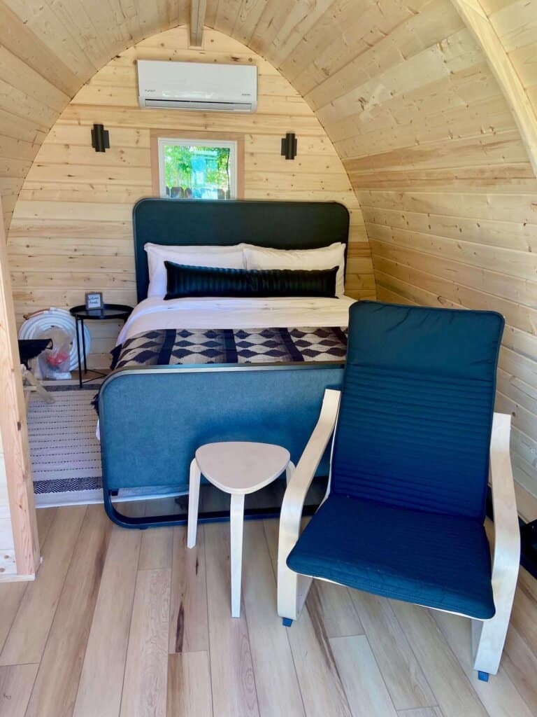 Wood paneled glamping pod with double bed and chair at the Bike Inn Bentonville