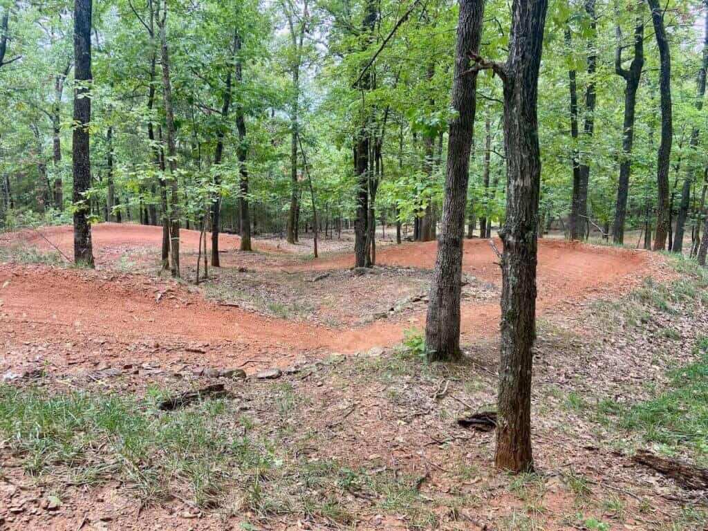 Switchbacked mountain bike trail with red dirt descending through forest in Arkansas