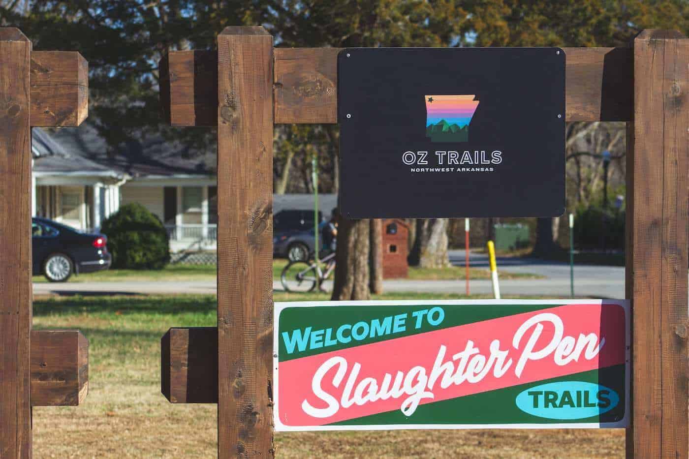 Two signs on fence in Bentonville Arkansas. One reads "Oz Trails" and the other reads "Slaughter Pen Trails"