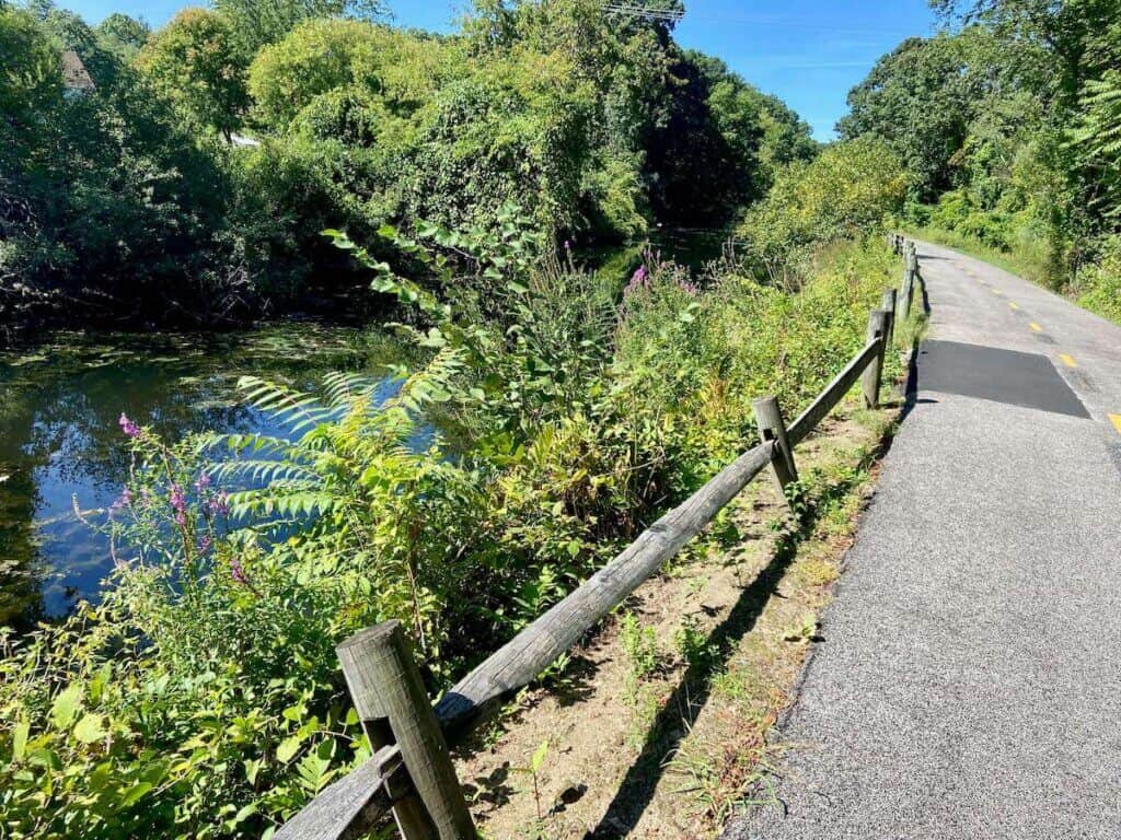 Blackstone River Bikeway multi-use path lined with vegetation and slow moving river